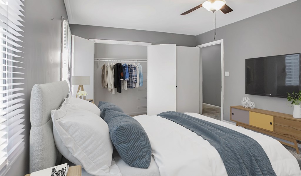 A bedroom with a bed, pillows, a ceiling fan, a mirror, a TV, and a window with blinds.