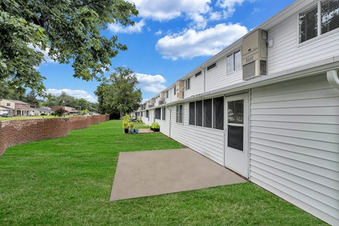 A grassy area in front of a building with a brick wall on the left.