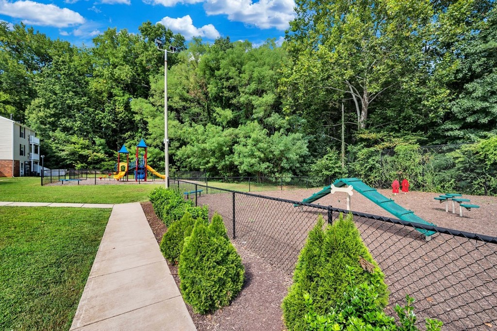 a park with a playground and a chain link fence     and trees