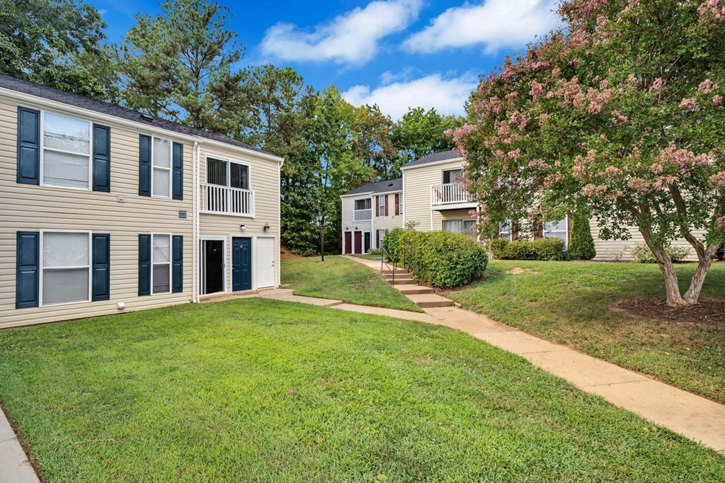 a sidewalk between two apartment buildings with grass and trees