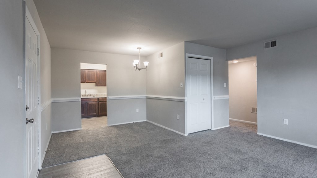 an empty living room with a door to a kitchen