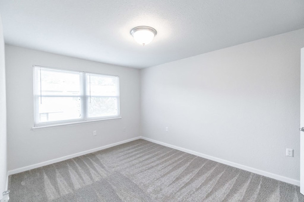 an empty living room with a window and carpet