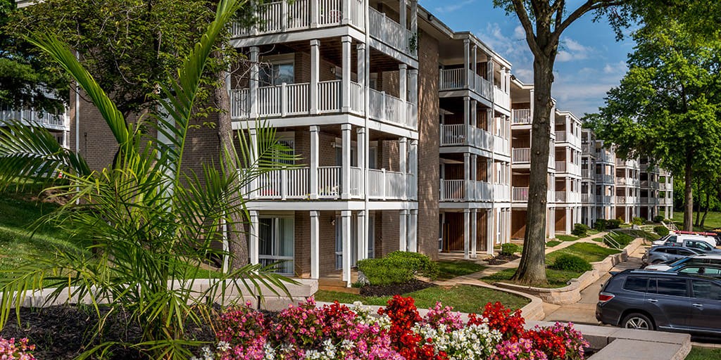 a picture of an apartment complex with trees and flowers in the foreground