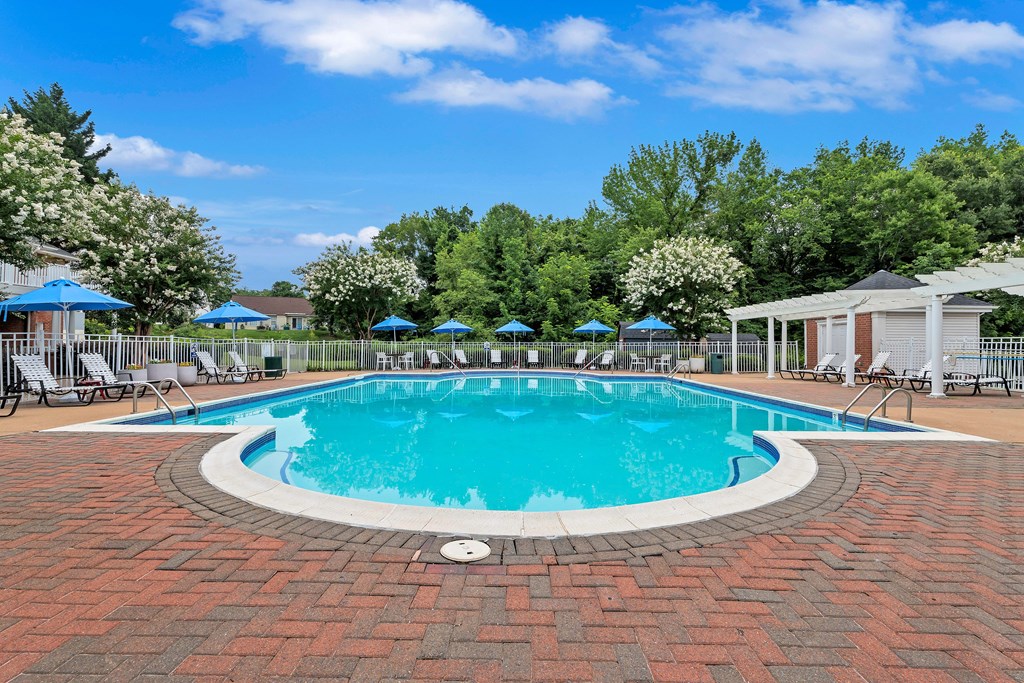 A round pool surrounded by red brick and blue umbrellas.