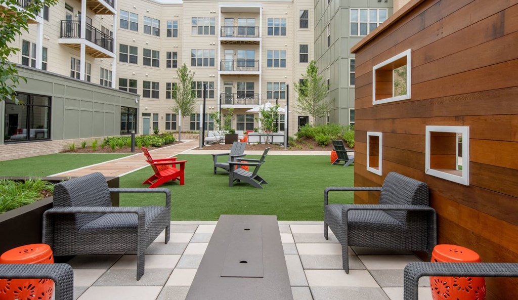 an outdoor lounge area with chairs and tables in front of an apartment building