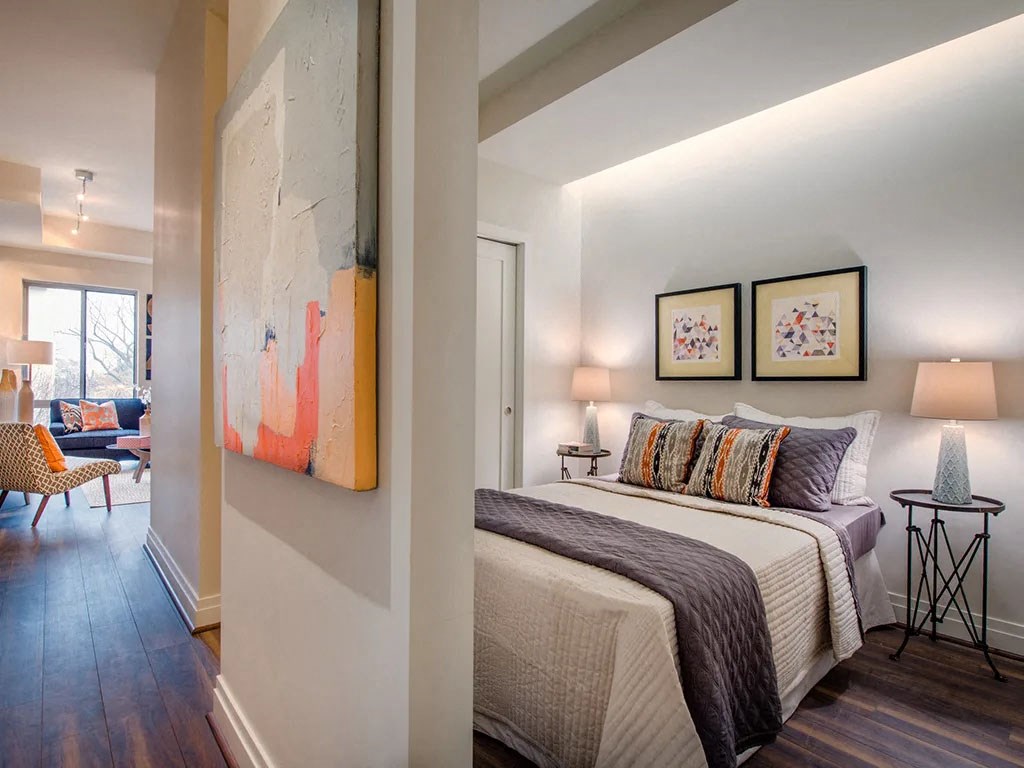 a bedroom with a bed and a hallway to a living room