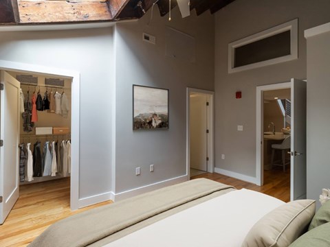 A bedroom with a large bed and a closet with clothes hanging.