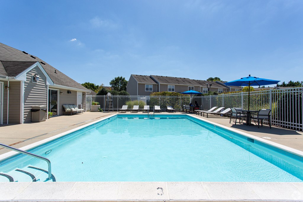 A swimming pool surrounded by a white fence and blue umbrellas.