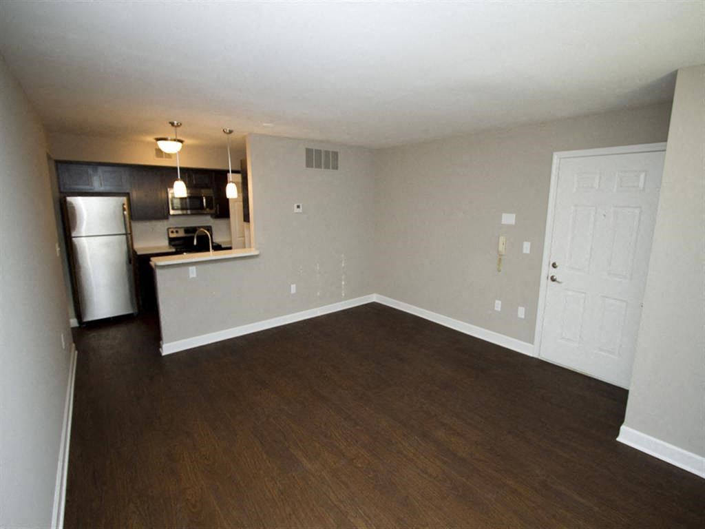 an empty living room with a kitchen in the background