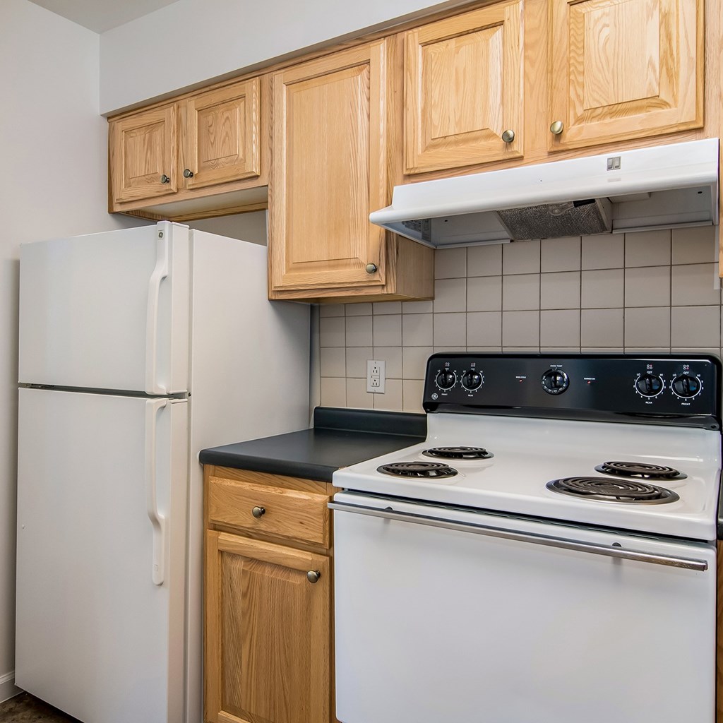 A kitchen with a white refrigerator, white stove, and wooden cabinets.
