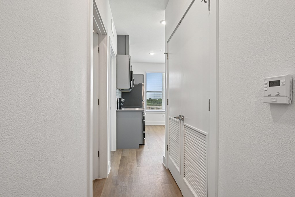 A white hallway with a door on the right and a kitchen area in the background.