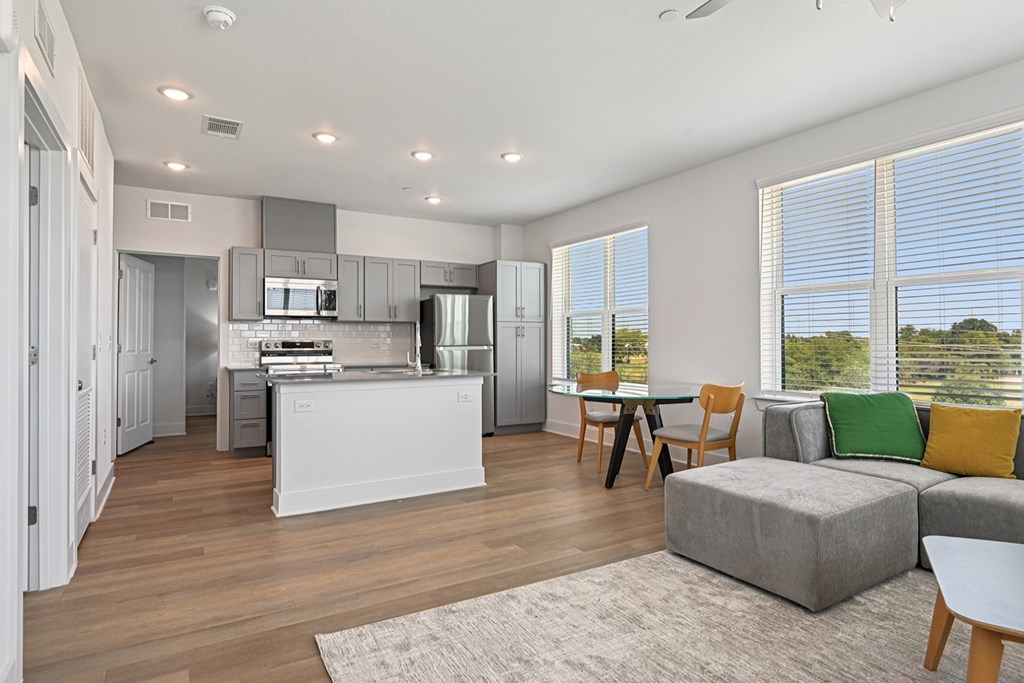 A modern kitchen with a breakfast bar and a living area with a grey sofa.