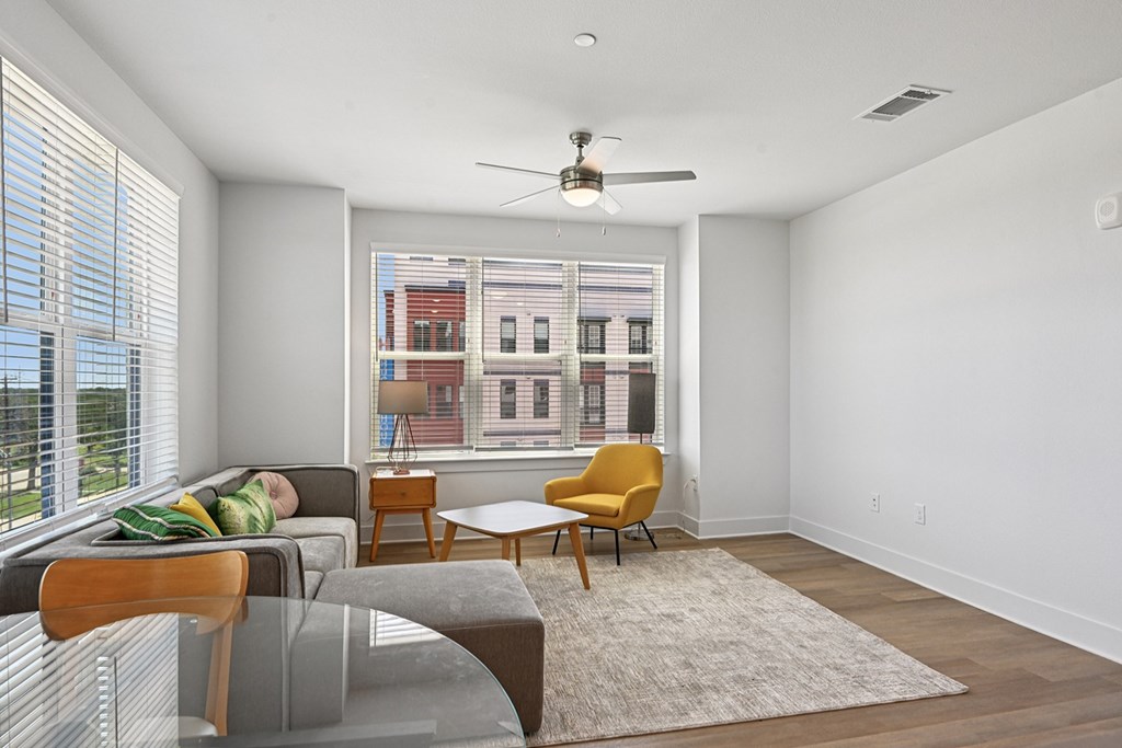 A living room with a grey couch, a yellow chair, a grey table and a window with blinds.