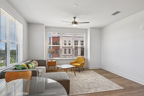 A living room with a grey couch, a yellow chair, a grey table and a window with blinds.