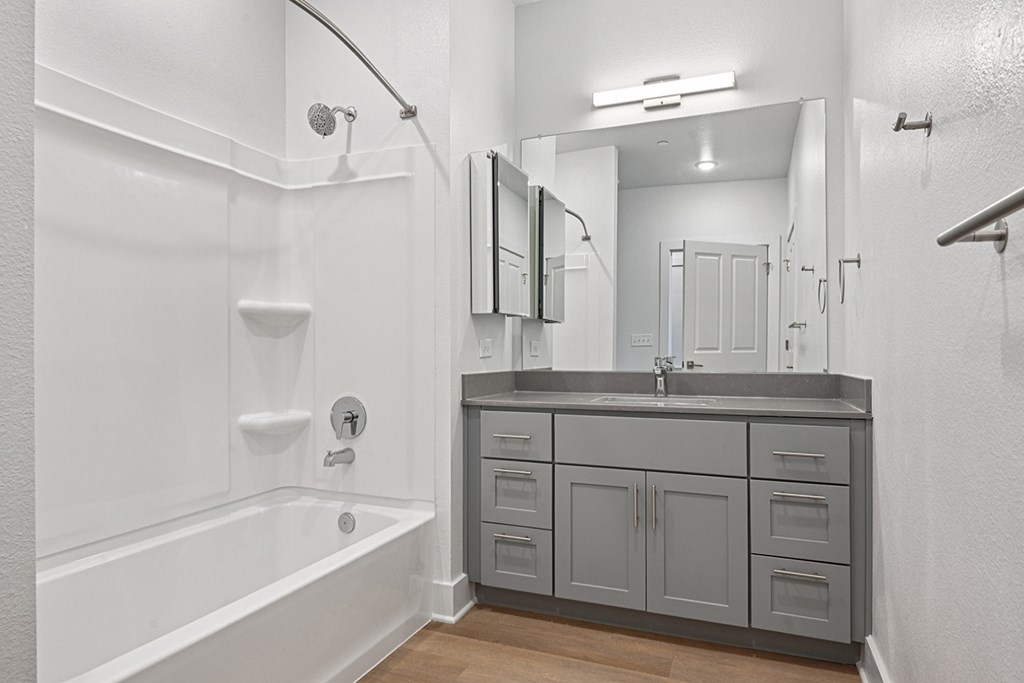 A white bathroom with a tub, sink, and mirror.