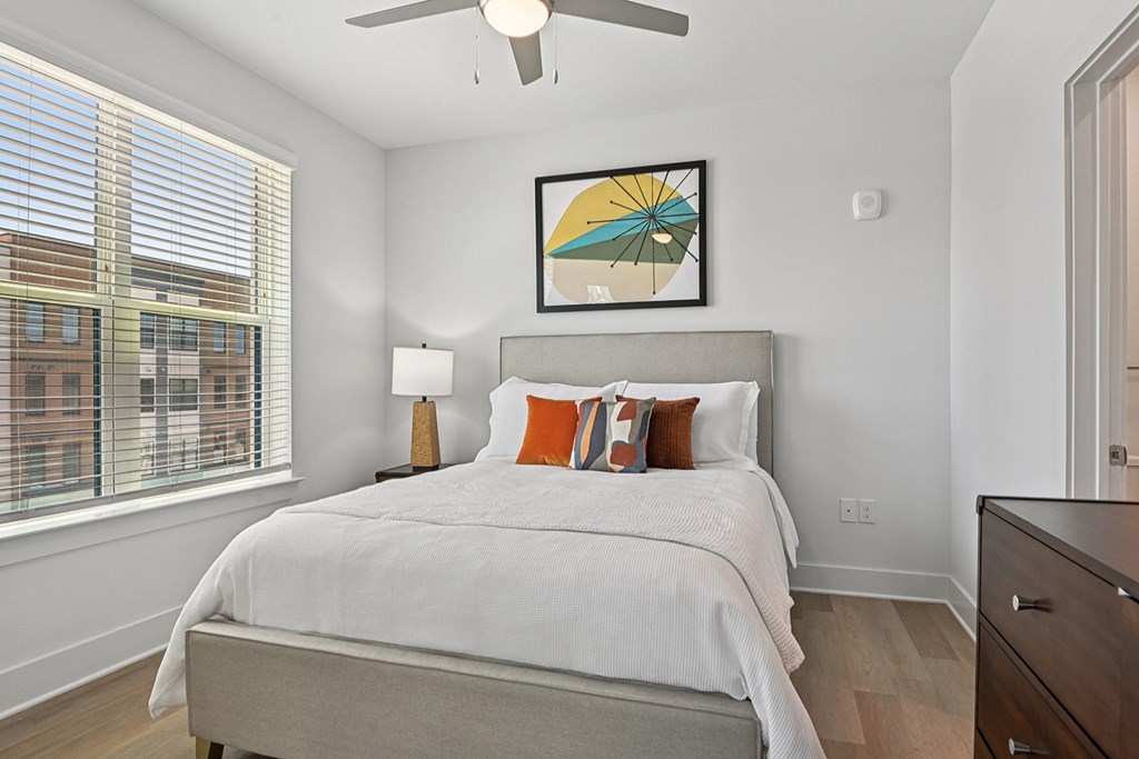 A bedroom with a bed, a ceiling fan, and a painting on the wall.