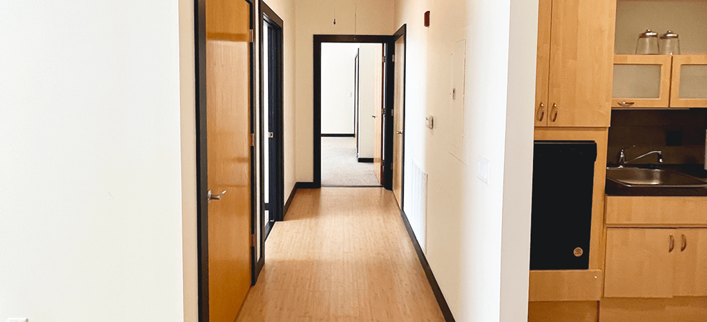 a hallway in an apartment with wood floors and white walls and a door open to a bedroom