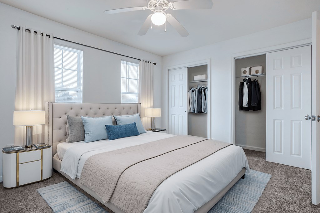 A bedroom with a large bed, a ceiling fan, and a closet with clothes hanging.