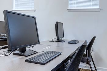 A black computer monitor and keyboard on a desk with a black chair.