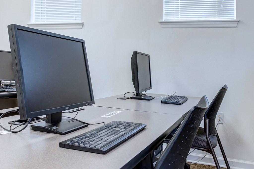 A black computer monitor and keyboard on a desk with a black chair.