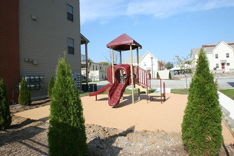 a playground with a red swing set in front of a house
