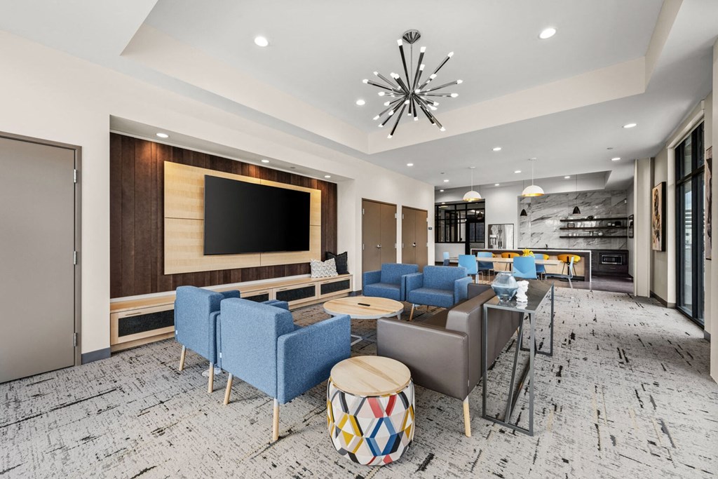 A modern living room with a large flat screen TV, blue chairs, and a wooden coffee table.