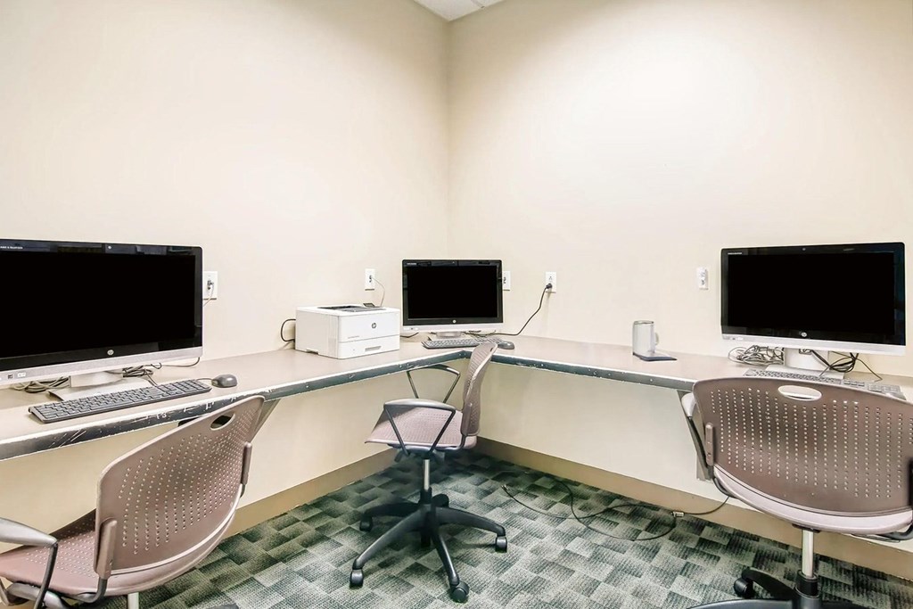 A room with a desk, chairs and computer monitors.
