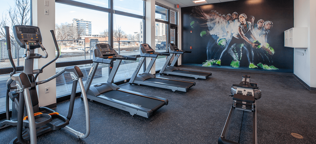 a gym with cardio equipment and a wall mural of athletes