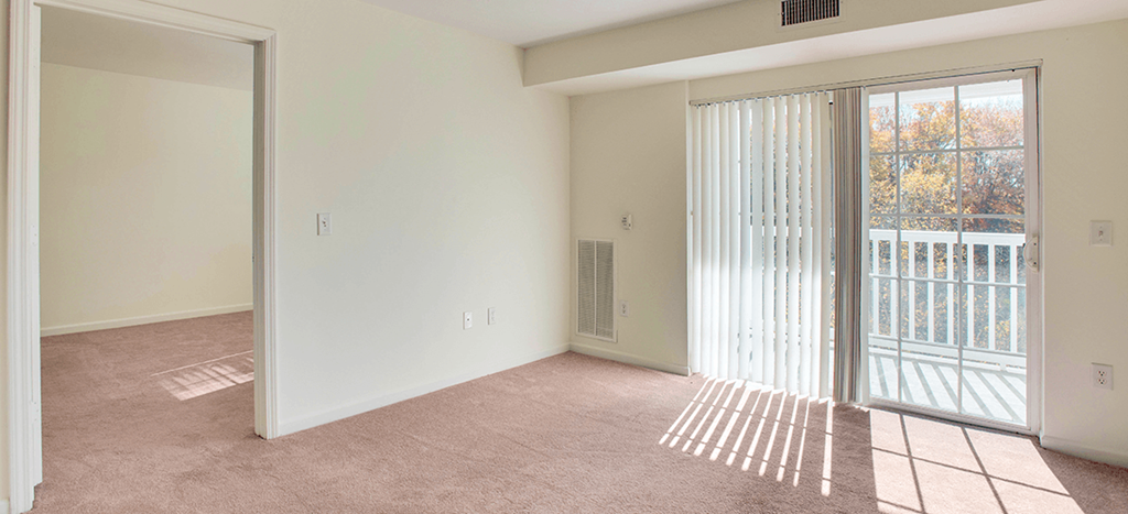 an empty living room with a sliding glass door to a balcony