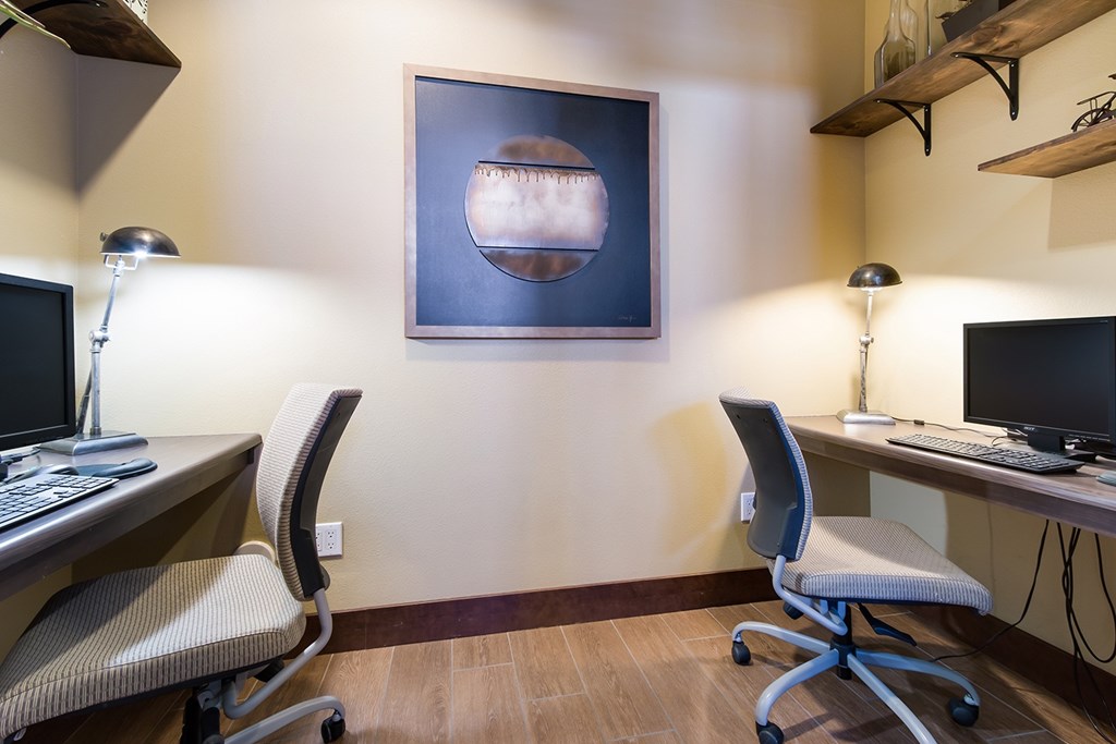 A room with two computers and a painting on the wall.