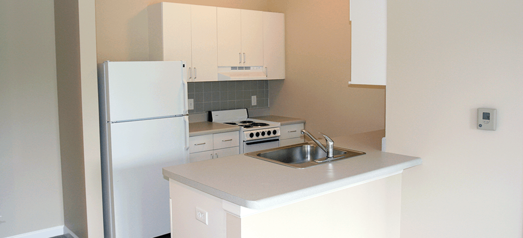 a kitchen at Cahill House apartments with white cabinets and a sink and a refrigerator