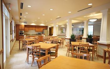 a dining room with tables and chairs and a kitchen at Senior Living at Cambridge Heights