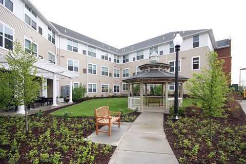 a courtyard with a gazebo and benches in front of an apartment building at Cambridge Senior Living
