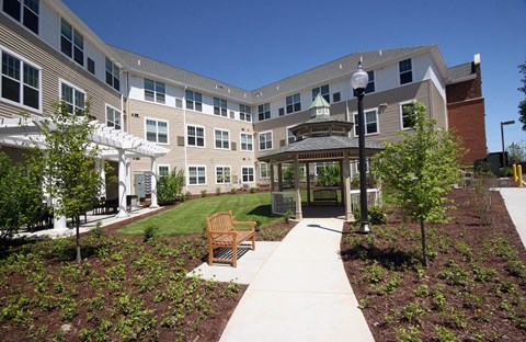 a courtyard with a gazebo and benches in front of an apartment building at Cambridge Senior Living