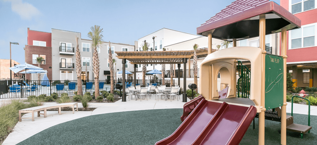 a playground with a slide in front of a pool area at Cedars at Carver Park apartments
