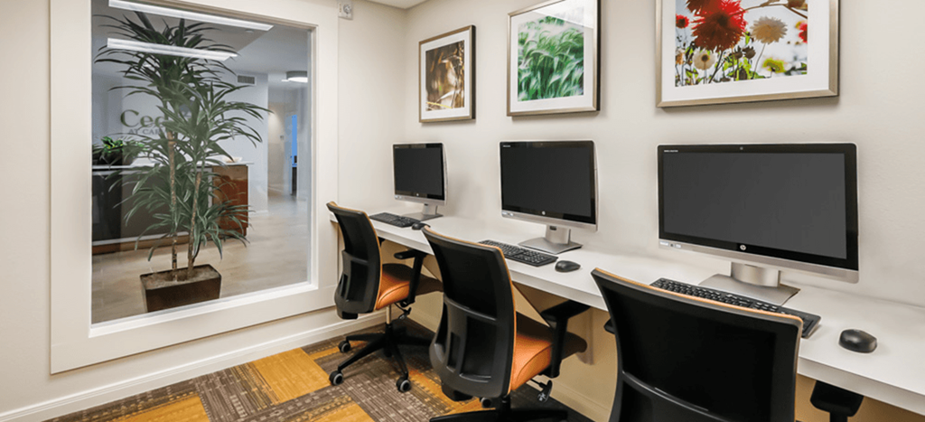 three computers sitting on a desk in a room at Cedars at Carver Park apartments