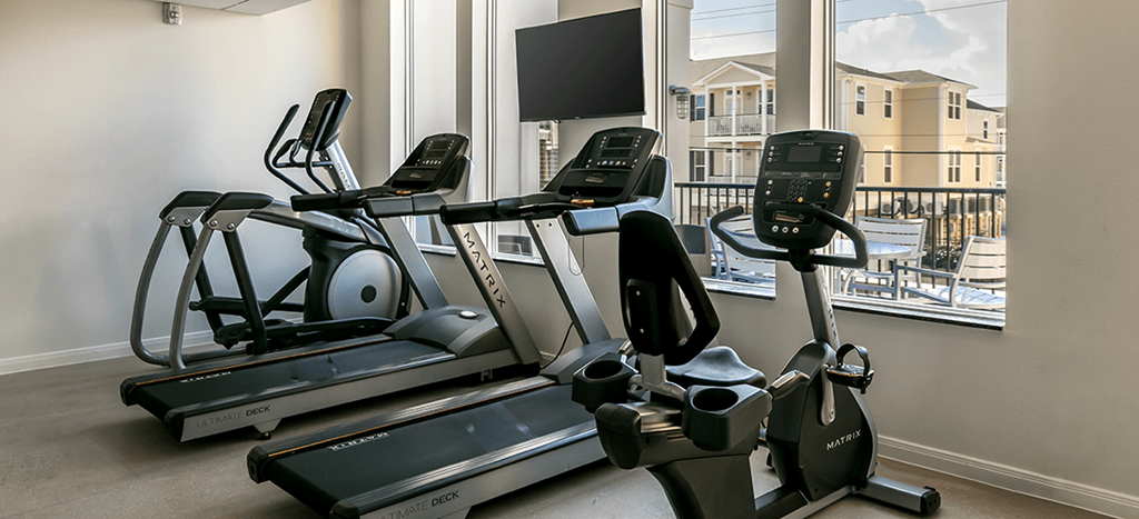 a gym with treadmills and a tv in a window