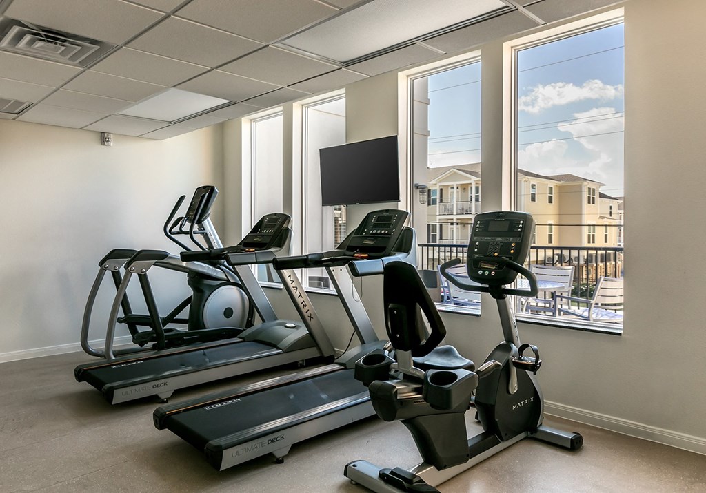 a gym with treadmills and a tv in front of a window