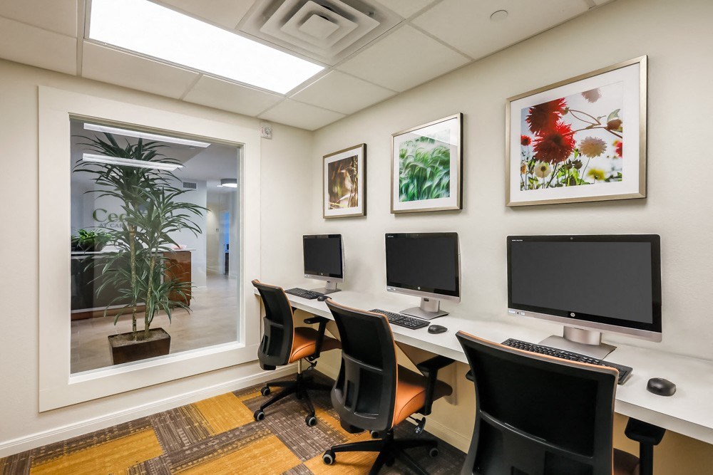a computer room with three monitors on a table and chairs