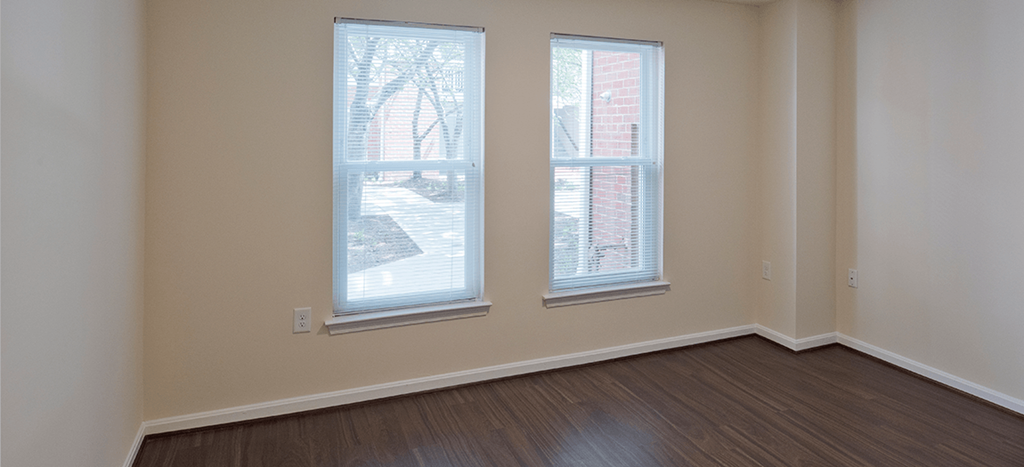 an empty bedroom with two windows and wood flooring