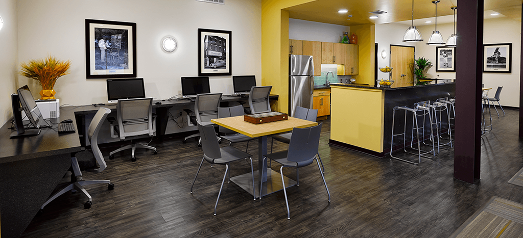 a computer room with desks and chairs and a kitchen with a yellow counter