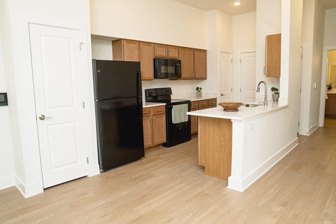 A black refrigerator is in the corner of a kitchen with wooden cabinets.