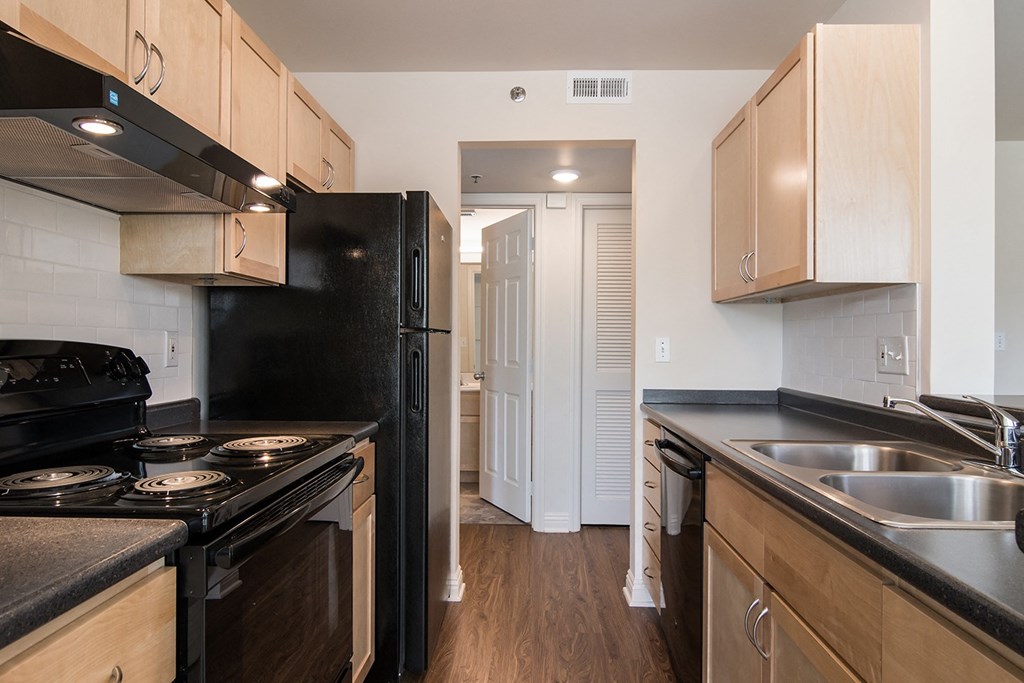 a kitchen with black appliances and wooden cabinets and a door to a hallway at Crawford Square Apartments & Townhomes