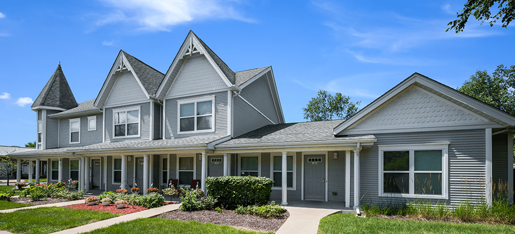 a gray apartment building with three pointed roofs and a sidewalk in front of it