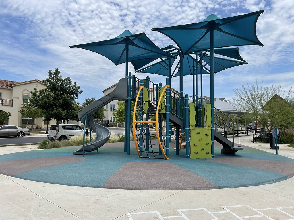 a playground with a swing set and umbrellas at East Meadows Apartments