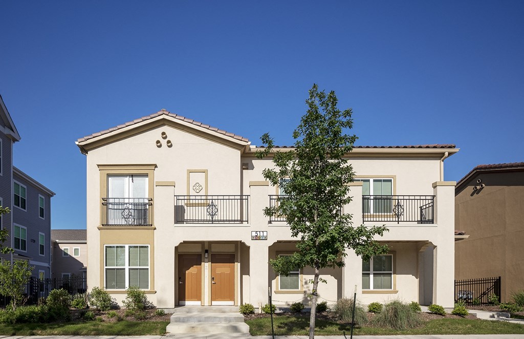 a townhouse with two balconies and a tree in front of it at East Meadows Apartments