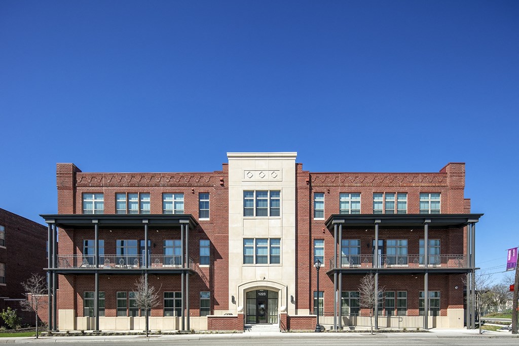 a red brick building on a street with a blue sky at East Meadows Apartments