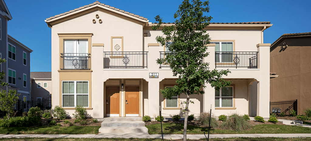 a beige apartment home with a tree in front of it