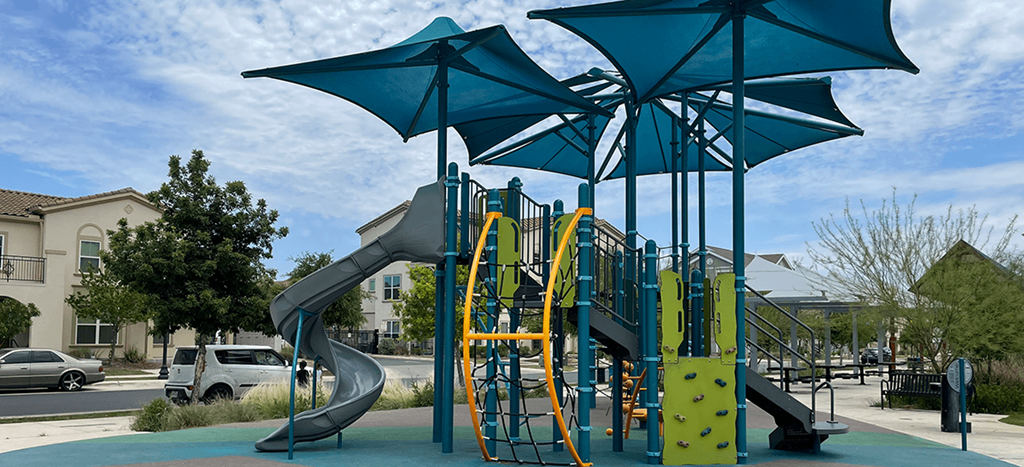 a playground with a slide and umbrella at East Meadows Apartments