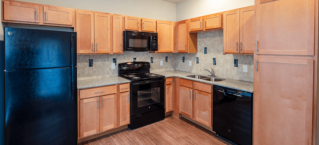 a kitchen with black appliances and wooden cabinets at East Meadows Apartments